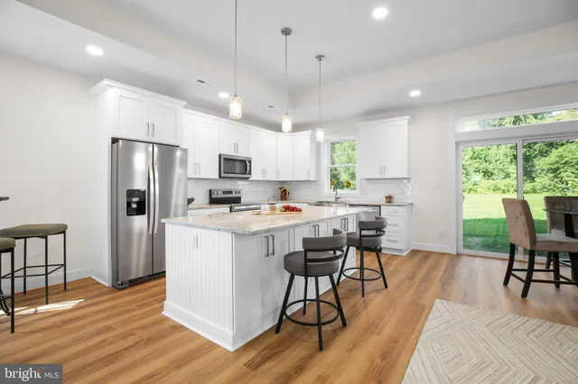 a kitchen with stainless steel appliances granite countertop a refrigerator a stove top oven a sink dishwasher a dining table and chairs with wooden floor