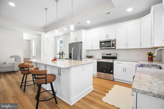 a kitchen with stainless steel appliances granite countertop a stove top oven a sink a refrigerator and white cabinets with wooden floor