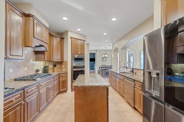 a kitchen with stainless steel appliances granite countertop a refrigerator a stove and a sink with wooden floor