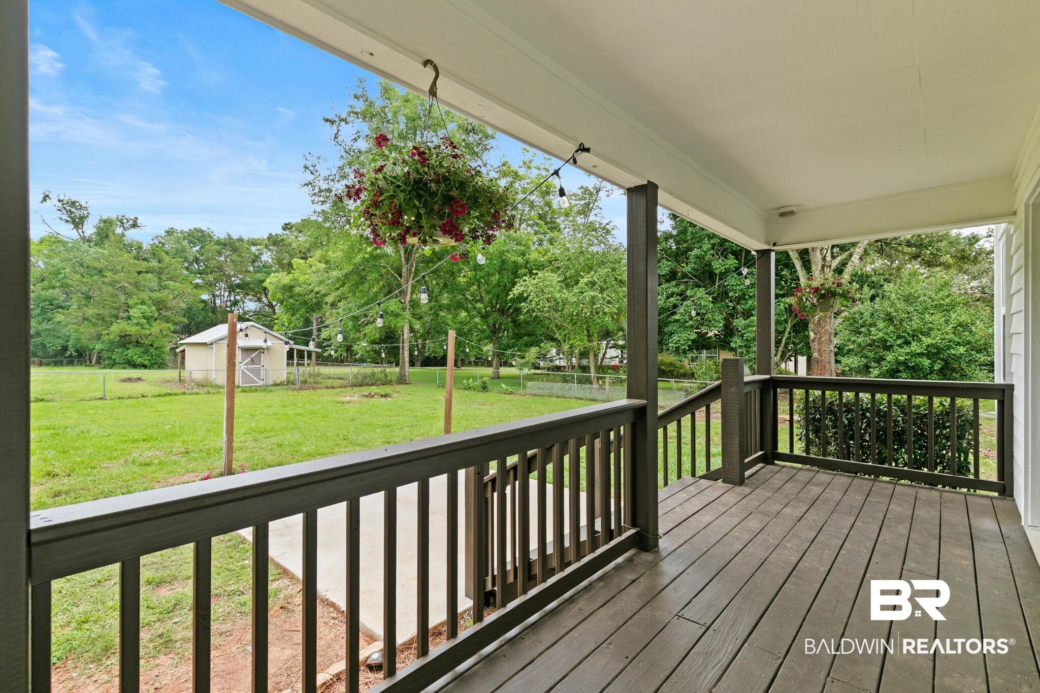 22810 High Ridge Road Fairhope, AL 36532 - Photo 62 of 78 Covered porch with wood-finish decking and railing, overlooking a expansive grassy area with mature trees and a detached shed structure