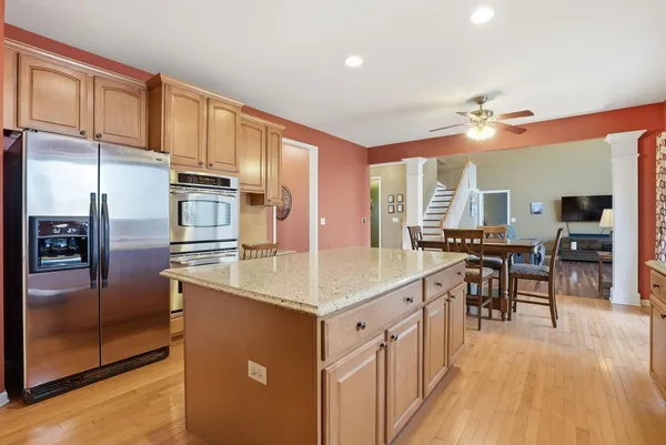 a kitchen with stainless steel appliances granite countertop a refrigerator a sink dishwasher a stove and a dining table with wooden floor