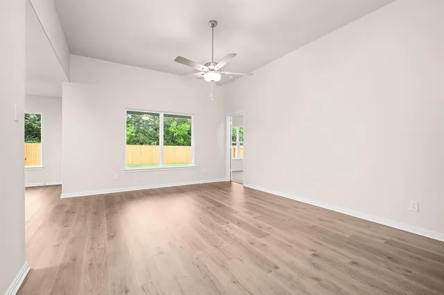 an empty room with wooden floor chandelier fan and windows