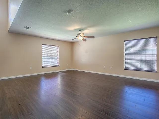 an empty room with wooden floor chandelier fan and windows