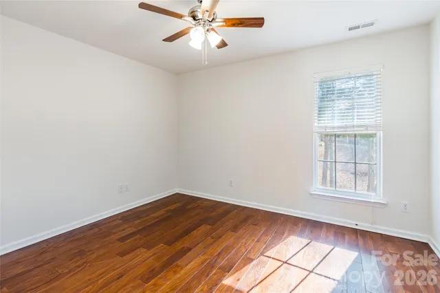 an empty room with wooden floor fan and windows