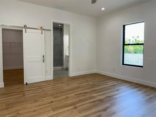 a view of an empty room with wooden floor and a ceiling fan