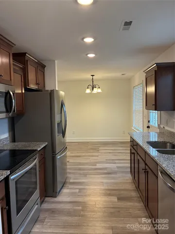 a kitchen with stainless steel appliances granite countertop a refrigerator a stove and a sink with wooden floor