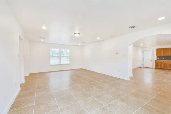 a view of an empty room with kitchen and a window