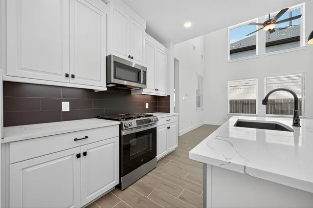 a kitchen with stainless steel appliances granite countertop a sink dishwasher a stove and a microwave oven with white cabinets