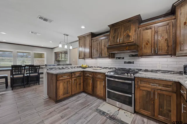 a kitchen with stainless steel appliances granite countertop wooden cabinets a sink dishwasher a stove and a refrigerator with wooden floor