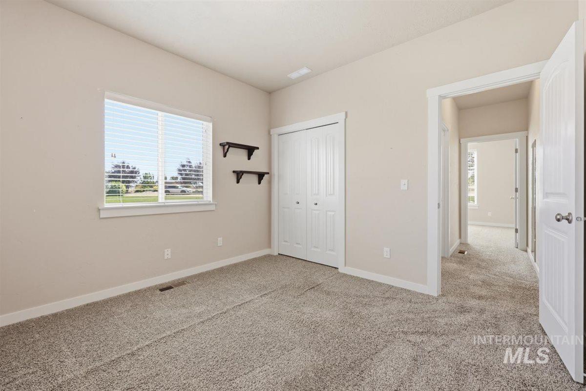 13496 Hockberger Ranch Road Caldwell, ID 83607 - Photo 9 of 40 Carpeted interior space featuring a window with white blinds, bi-fold closet doors, wall-mounted shelving, and neutral wall paint