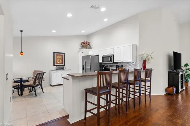 a kitchen with stainless steel appliances kitchen island granite countertop a dining table chairs and a refrigerator