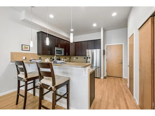 a kitchen with stainless steel appliances a dining table chairs refrigerator and microwave