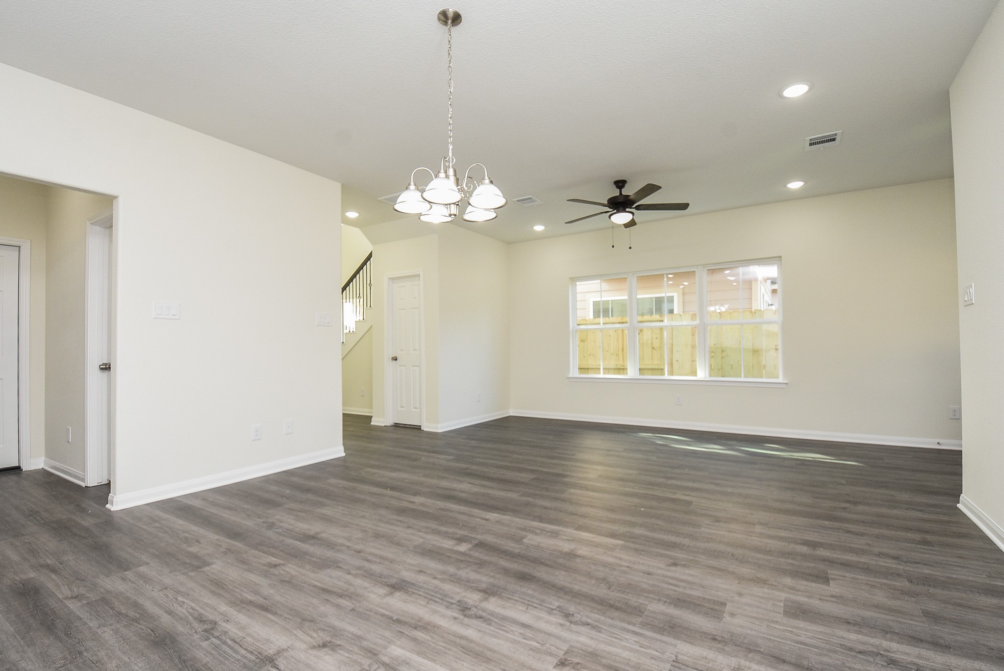 2811 Topiary Lane Houston, TX 77014 - Photo 10 of 32 Spacious, empty room with hardwood floors, neutral walls, ceiling fan, large windows, and a chandelier, in a modern home interior.
