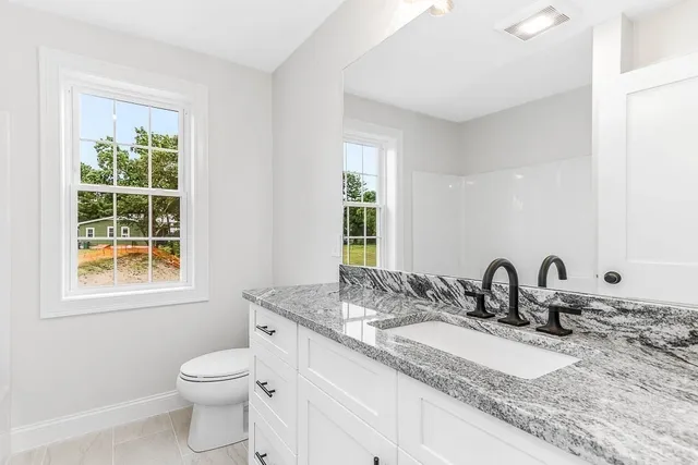 a bathroom with a granite countertop sink a toilet and a window