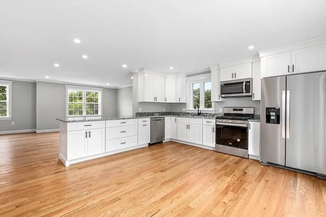 a kitchen with granite countertop a refrigerator oven a sink dishwasher and white cabinets with wooden floor