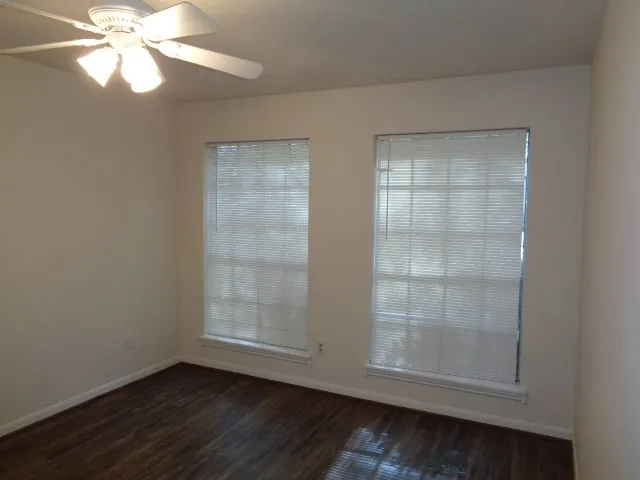 an empty room with wooden floor fan and windows