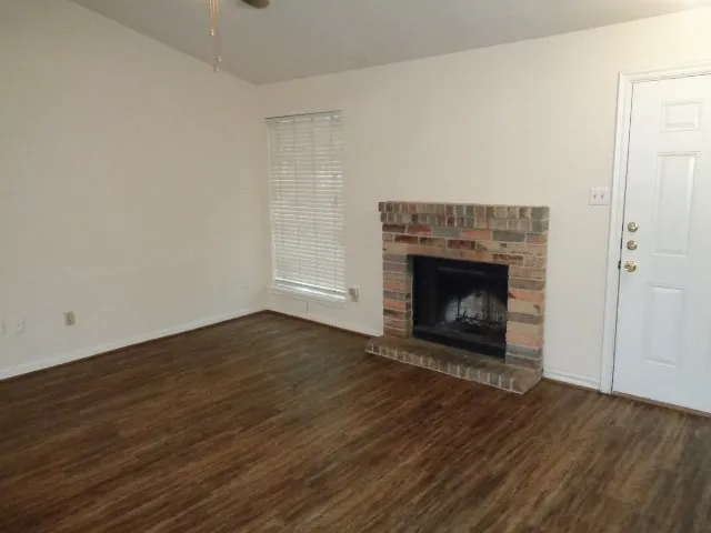 a view of an empty room with wooden floor fireplace and a window