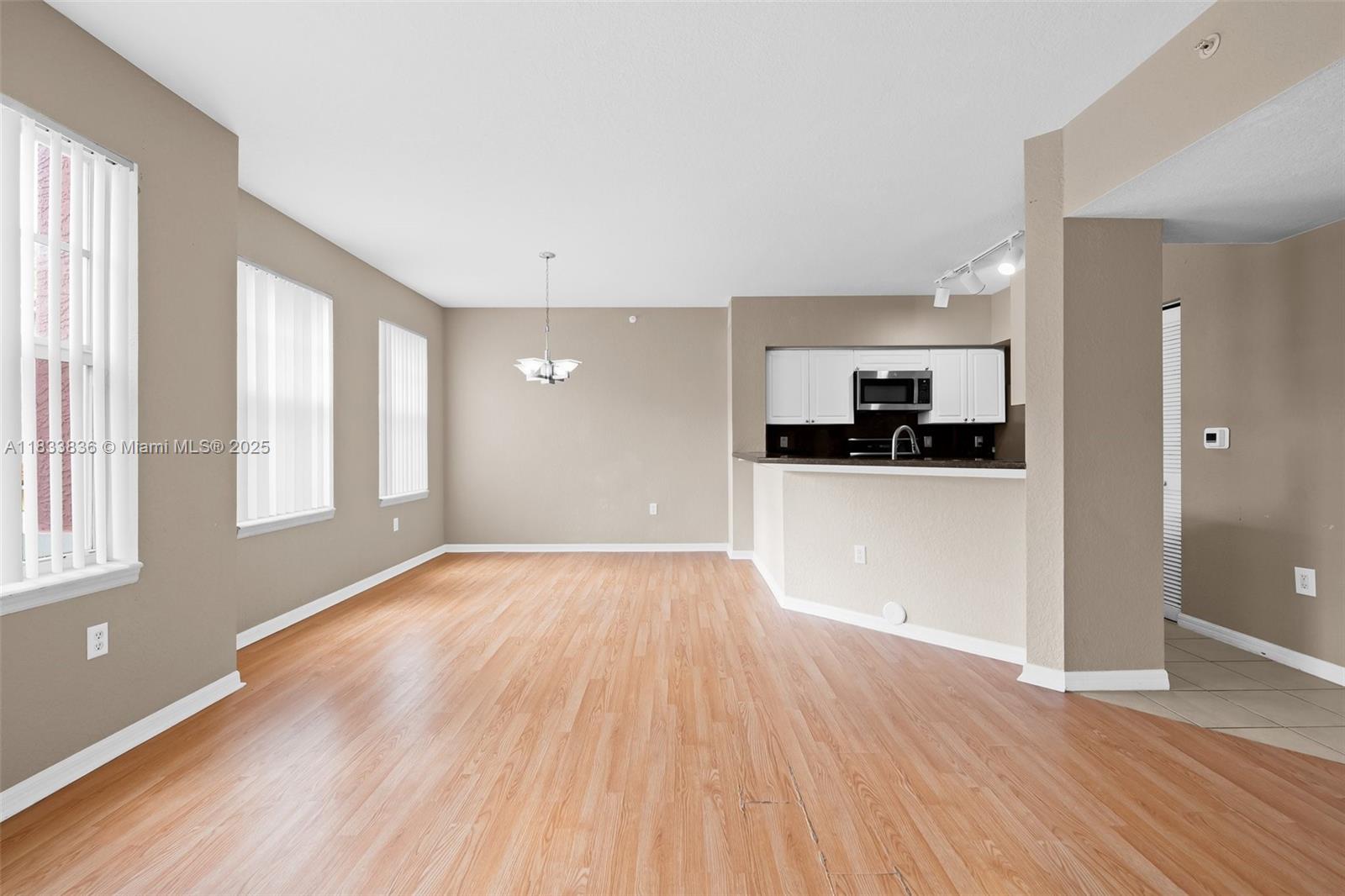 6722 West Sample Road, Unit 6722 Coral Springs, FL 33067 - Photo 4 of 23 a view of a kitchen and an empty room with wooden floor and a window