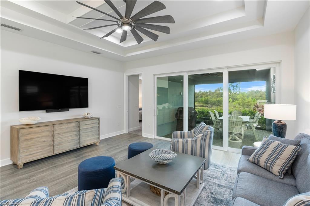 6847 Saona Court Naples, FL 34113 - Photo 7 of 47 a living room with furniture a flat screen tv and a floor to ceiling window
