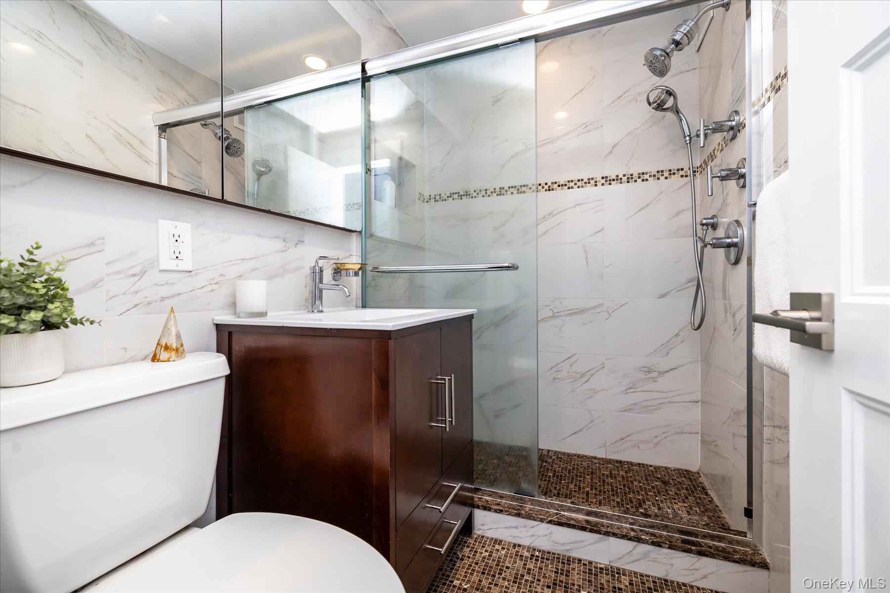 522 Shore Road, Unit 3BB Long Beach, NY 11561 - Photo 15 of 27 Bathroom featuring a walk-in shower with glass enclosure, white marble-look wall tiling, and pebble-style flooring