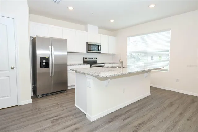 a kitchen with stainless steel appliances granite countertop a stove a refrigerator a sink a microwave and wooden floor