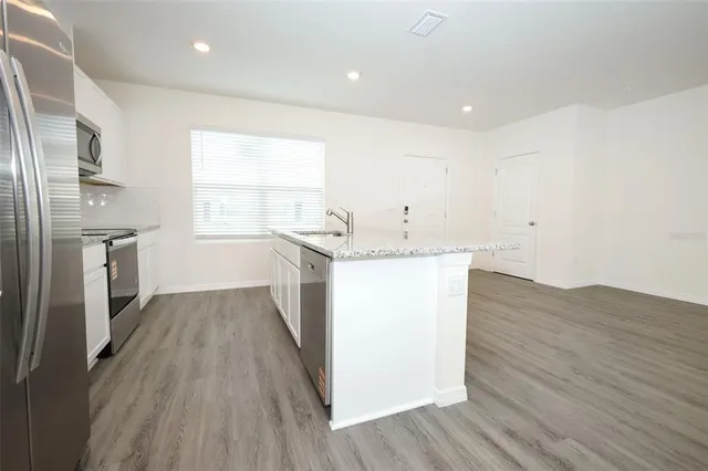 a kitchen with stainless steel appliances granite countertop a sink a stove a refrigerator and island with wooden floor