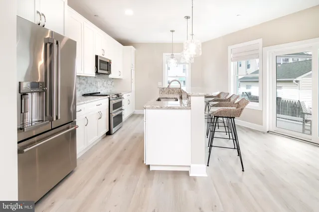 a kitchen with stainless steel appliances kitchen island granite countertop a refrigerator a stove a sink a dining table and chairs with wooden floor