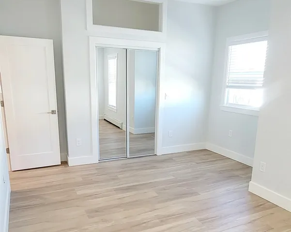 an empty room with wooden floor closet and windows