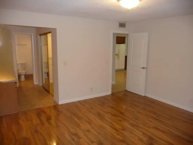 a view of an empty room with wooden floor and a bathroom