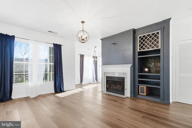a view of an empty room with wooden floor fireplace and a window