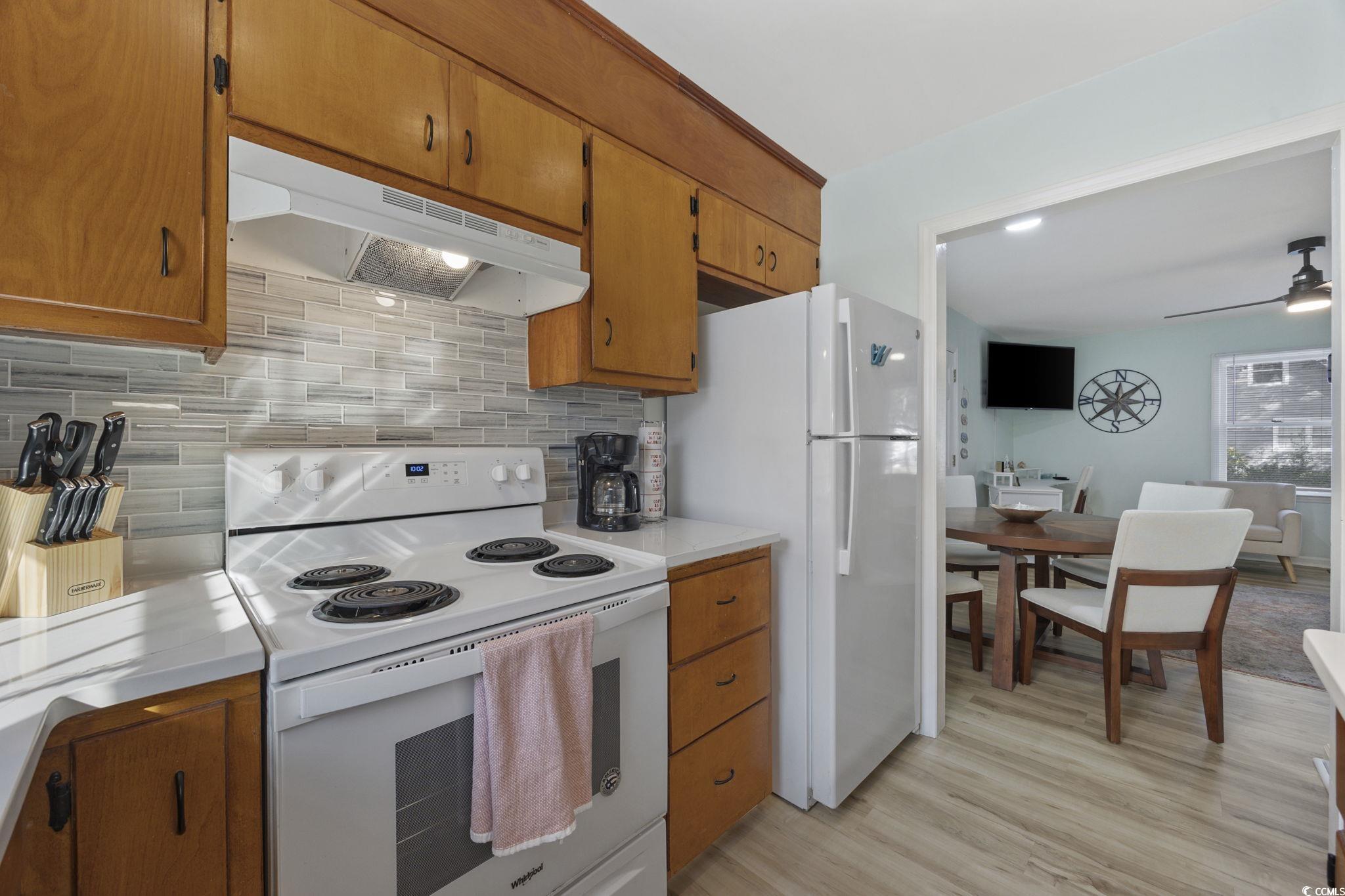 787 Causey Road Murrells Inlet, SC 29576 - Photo 11 of 40 Kitchen with white appliances, brown cabinetry, under cabinet range hood, light wood finished floors, and decorative backsplash