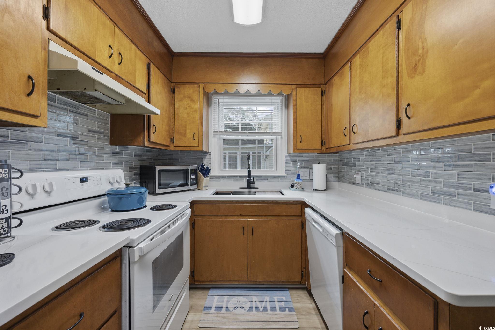 787 Causey Road Murrells Inlet, SC 29576 - Photo 27 of 40 Kitchen with white appliances, brown cabinetry, under cabinet range hood, and decorative backsplash