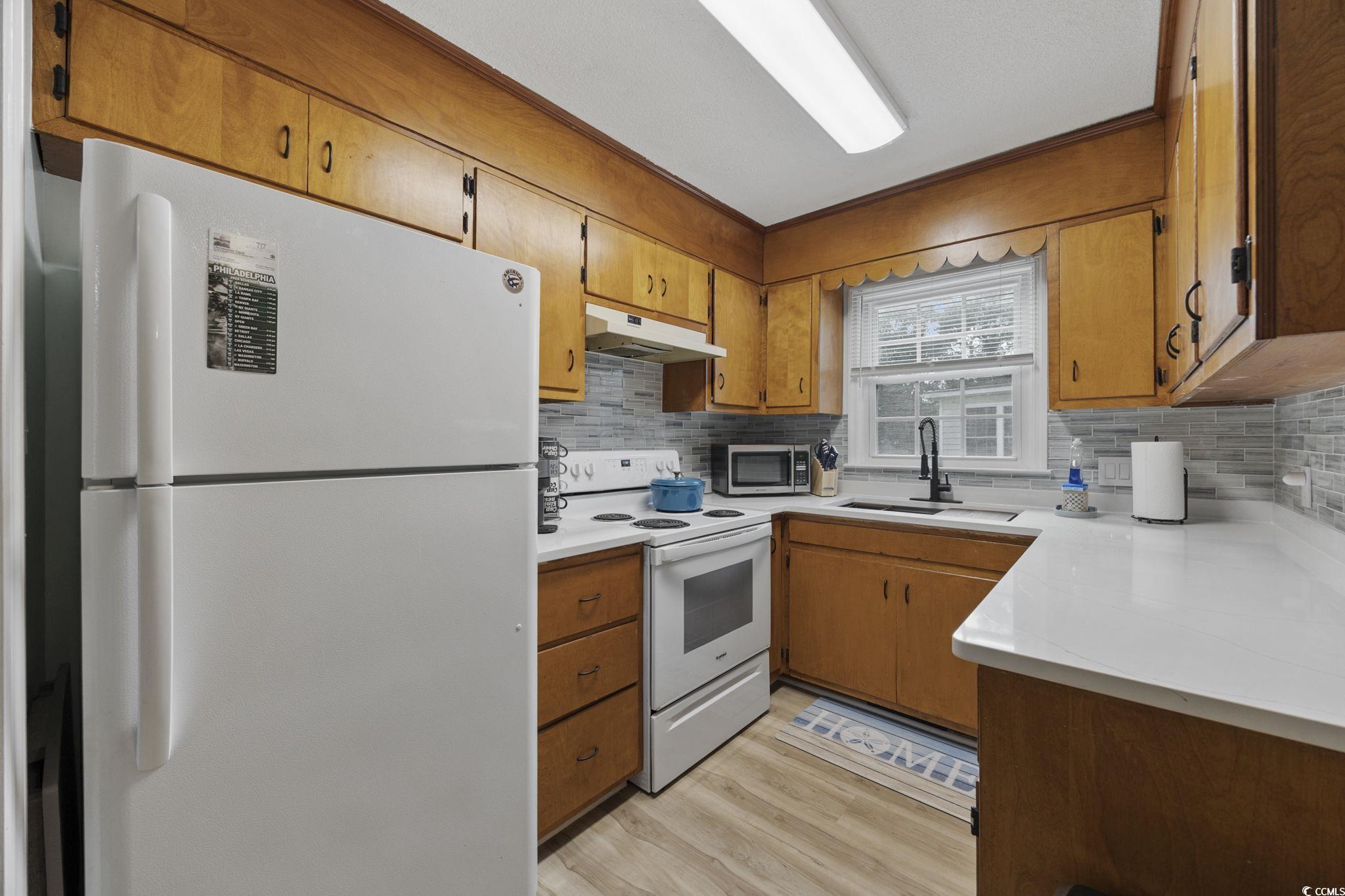787 Causey Road Murrells Inlet, SC 29576 - Photo 28 of 40 Kitchen with white appliances, brown cabinets, under cabinet range hood, decorative backsplash, and light wood-type flooring