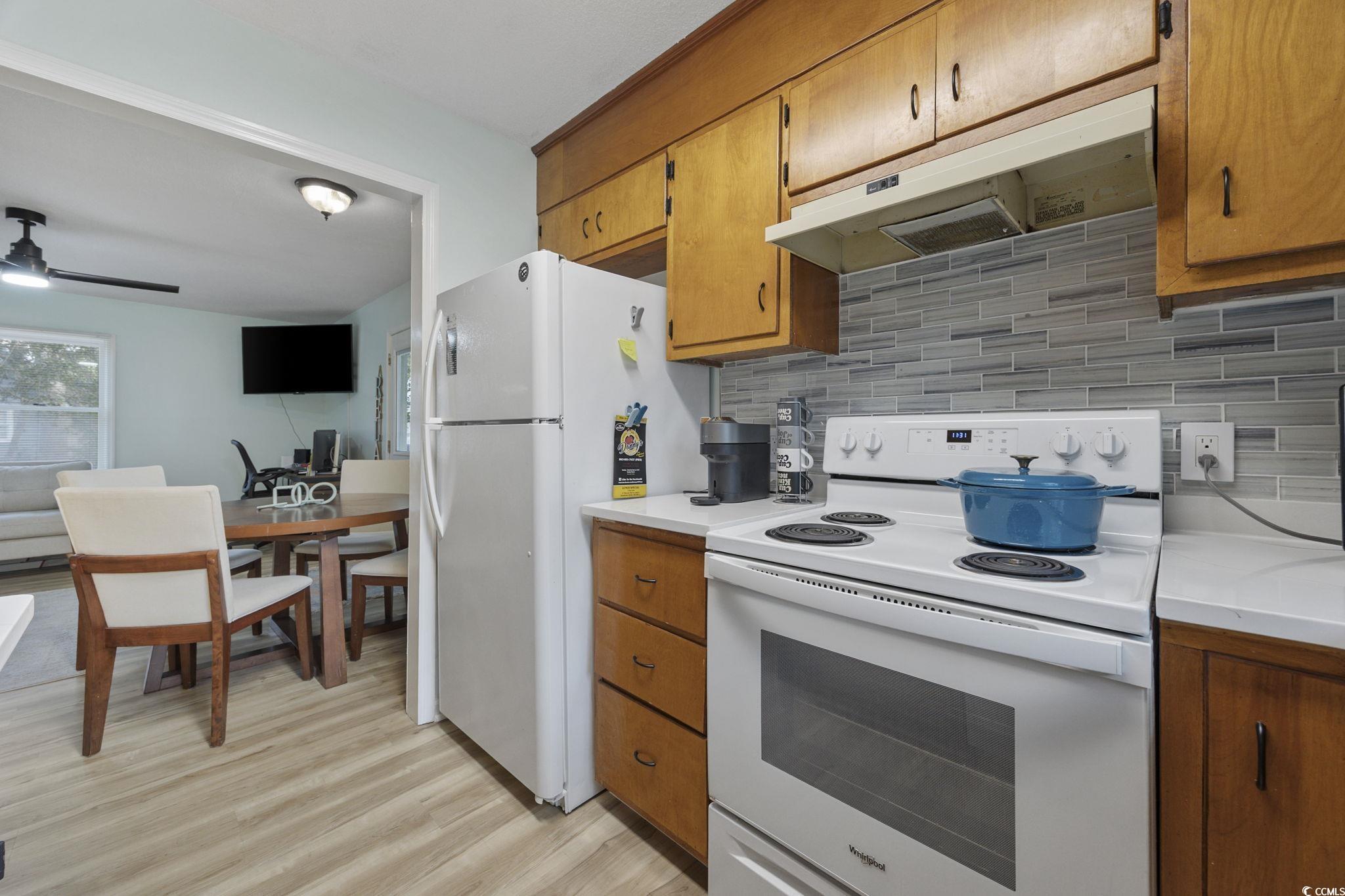 787 Causey Road Murrells Inlet, SC 29576 - Photo 29 of 40 Kitchen featuring white appliances, light countertops, brown cabinetry, under cabinet range hood, and decorative backsplash