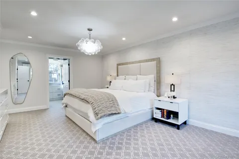a spacious bedroom with a bed a chandelier with vanity and mirror