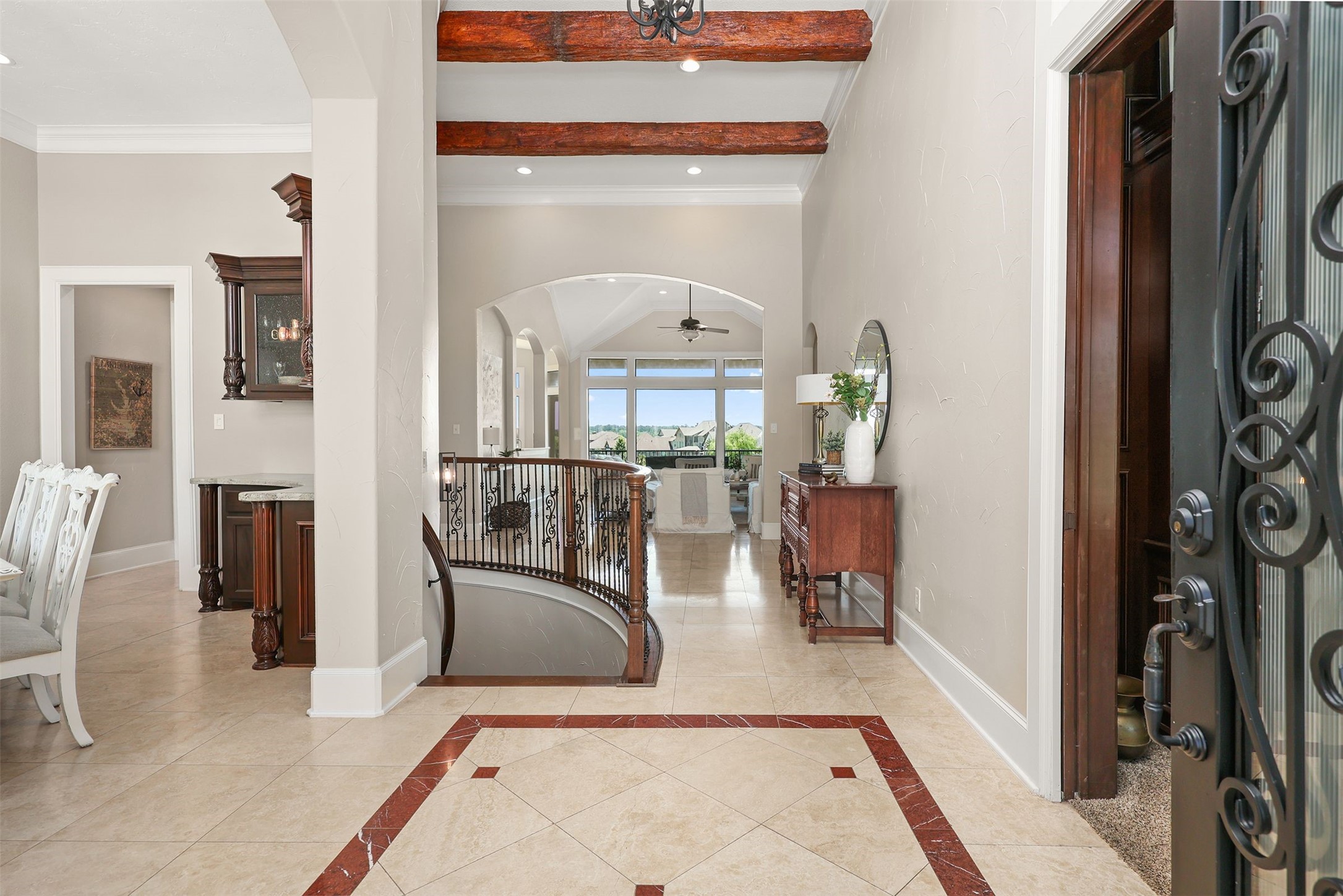 10896 Decatur Street Willis, TX 77318 - Photo 15 of 50 Step into a welcoming entryway with elegant tile flooring and wood beam accents, seamlessly leading to a bright and airy living area with large windows offering scenic views and a sophisticated staircase, all complemented by tasteful decor.
