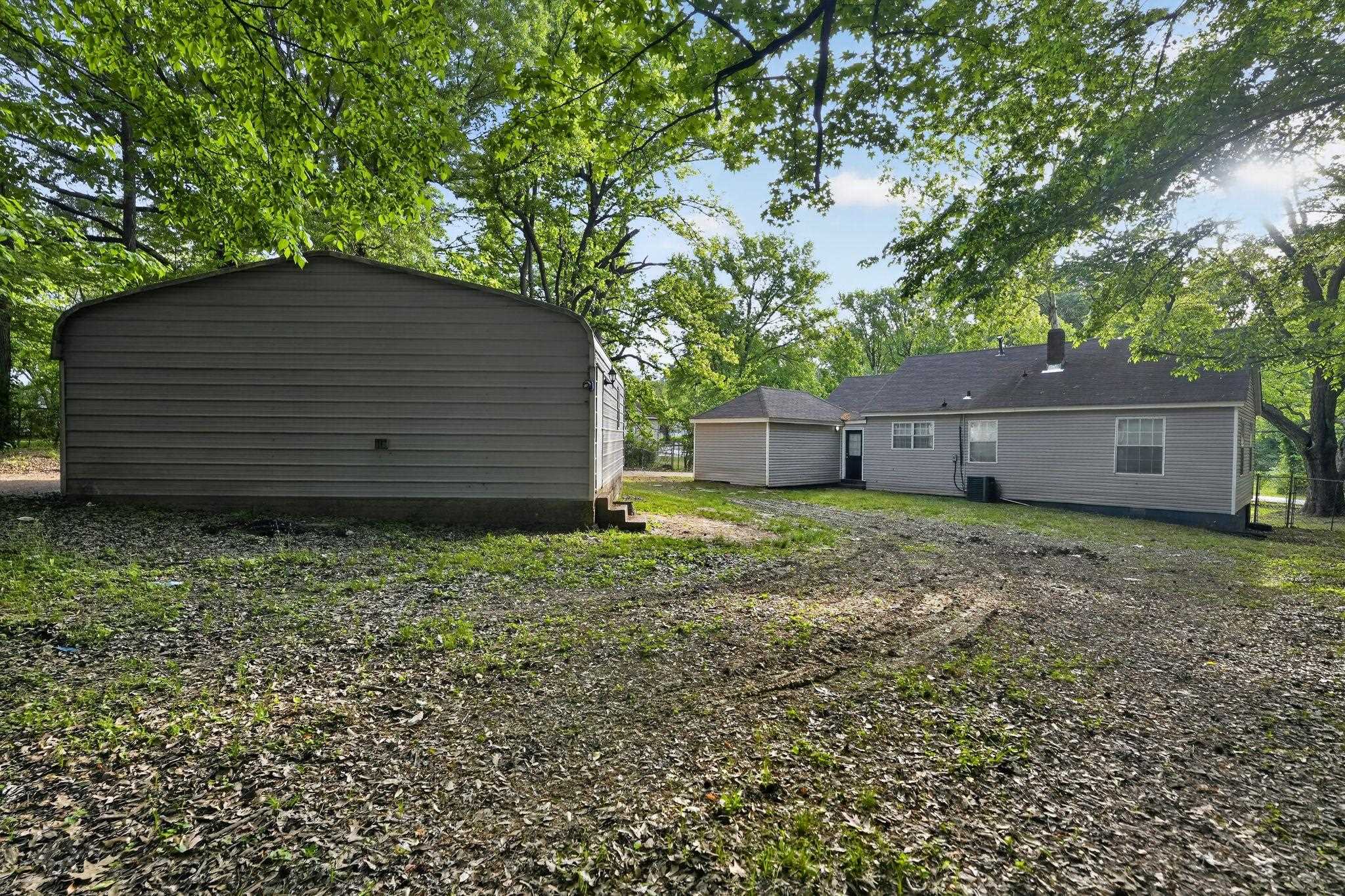 4199 Auburn Road Memphis, TN 38116 - Photo 30 of 32 Expansive backyard featuring a detached storage structure and a single-story residence with a grey siding exterior