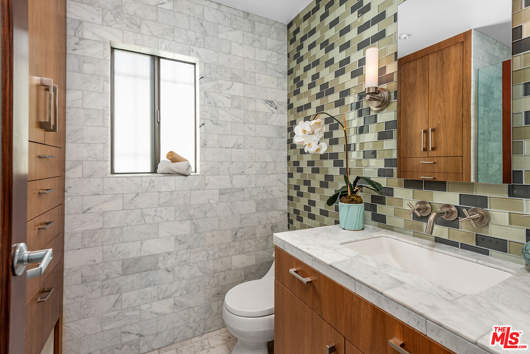 851 North Kings Road, Unit 307 West Hollywood, CA 90069 - Photo 29 of 38 a bathroom with a granite countertop toilet a sink and a mirror