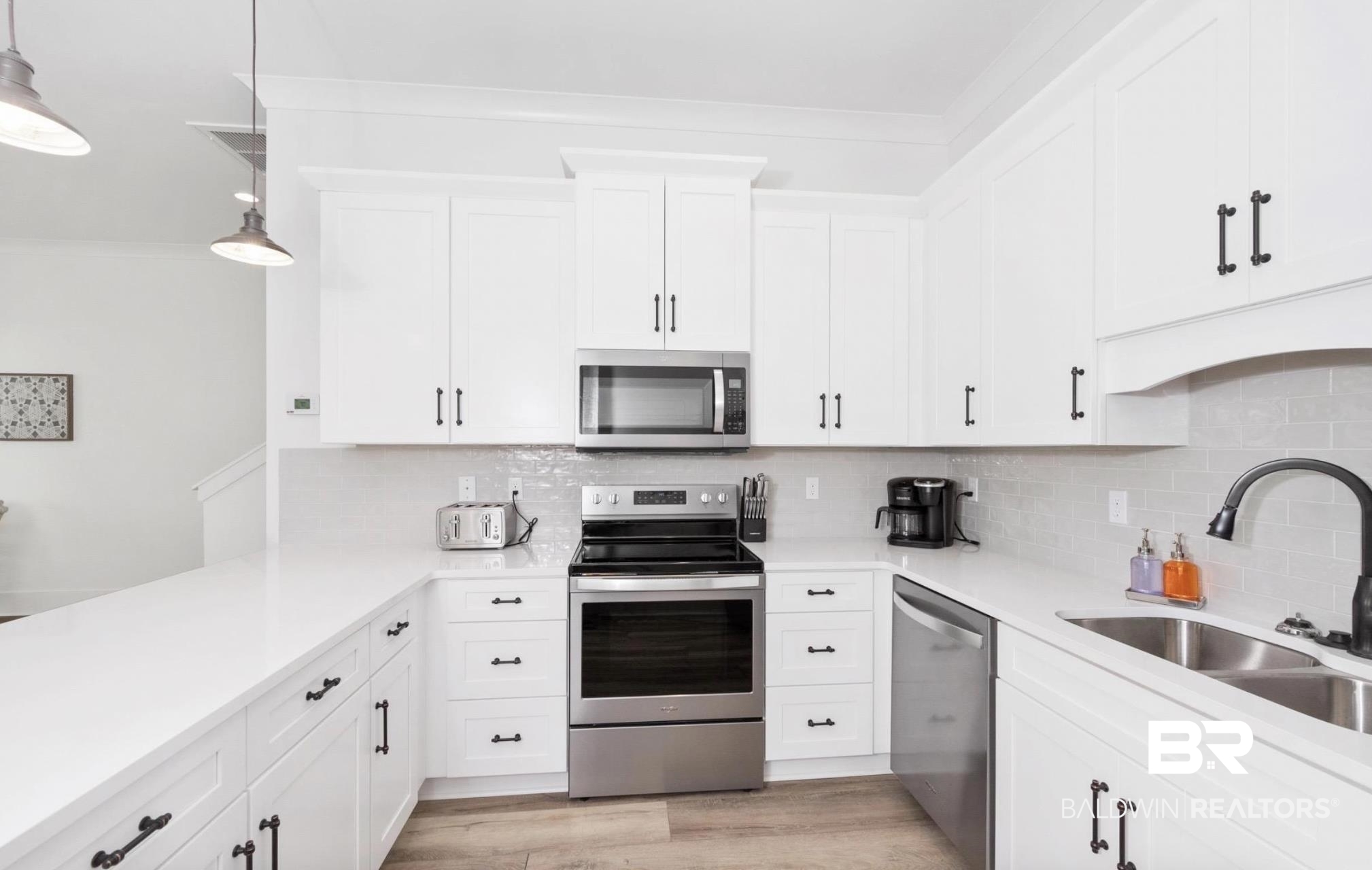 20 West Gate Orange Beach, AL 36561 - Photo 7 of 15 Kitchen with stainless steel appliances, white cabinetry, hanging light fixtures, and light wood-style flooring