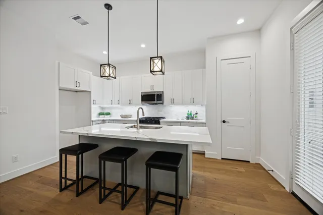 a kitchen with stainless steel appliances granite countertop a sink a stove a refrigerator and island with wooden floor