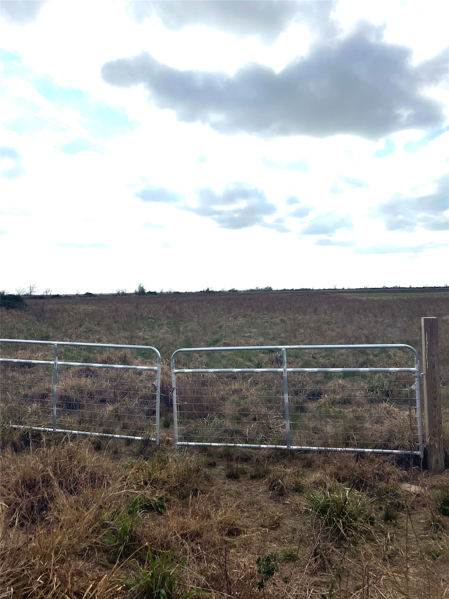 Expansive land featuring a metal gate entrance and a wooden fence post