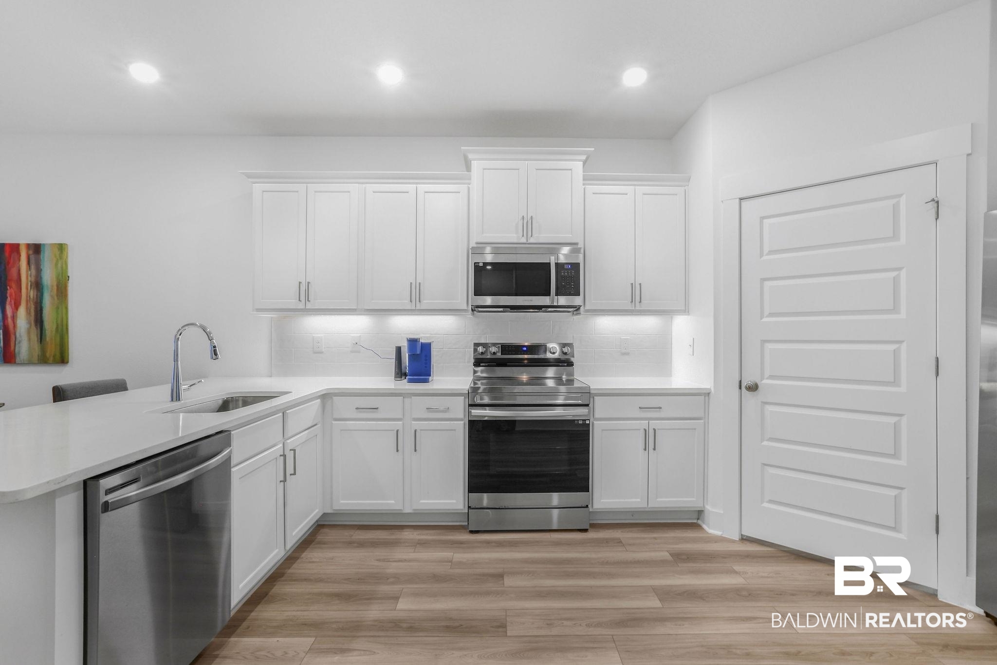 9859 Willet Way Foley, AL 36535 - Photo 5 of 23 Kitchen with white cabinetry, stainless steel appliances, a peninsula, backsplash, and light wood finished floors