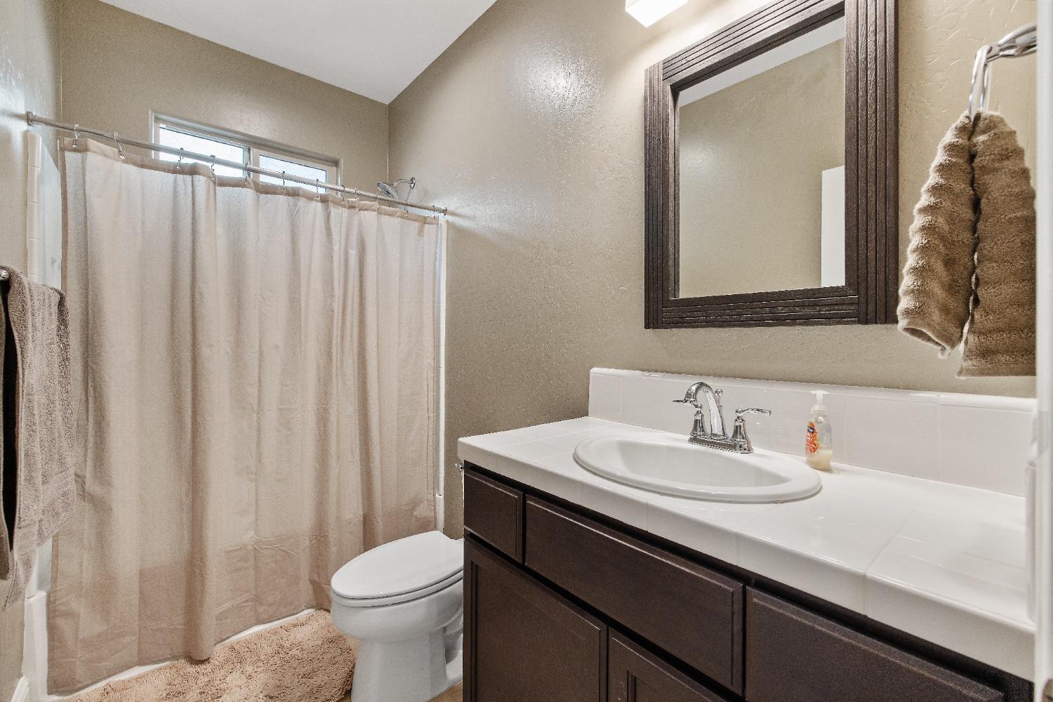 1210 Ridge Creek Estates Way Dinuba, CA 93618 - Photo 7 of 50 a bathroom with a sink a toilet and shower curtain
