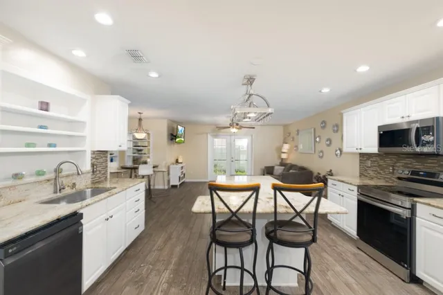 a open kitchen with stainless steel appliances granite countertop a stove top oven a sink dishwasher a dining table and chairs with wooden floor