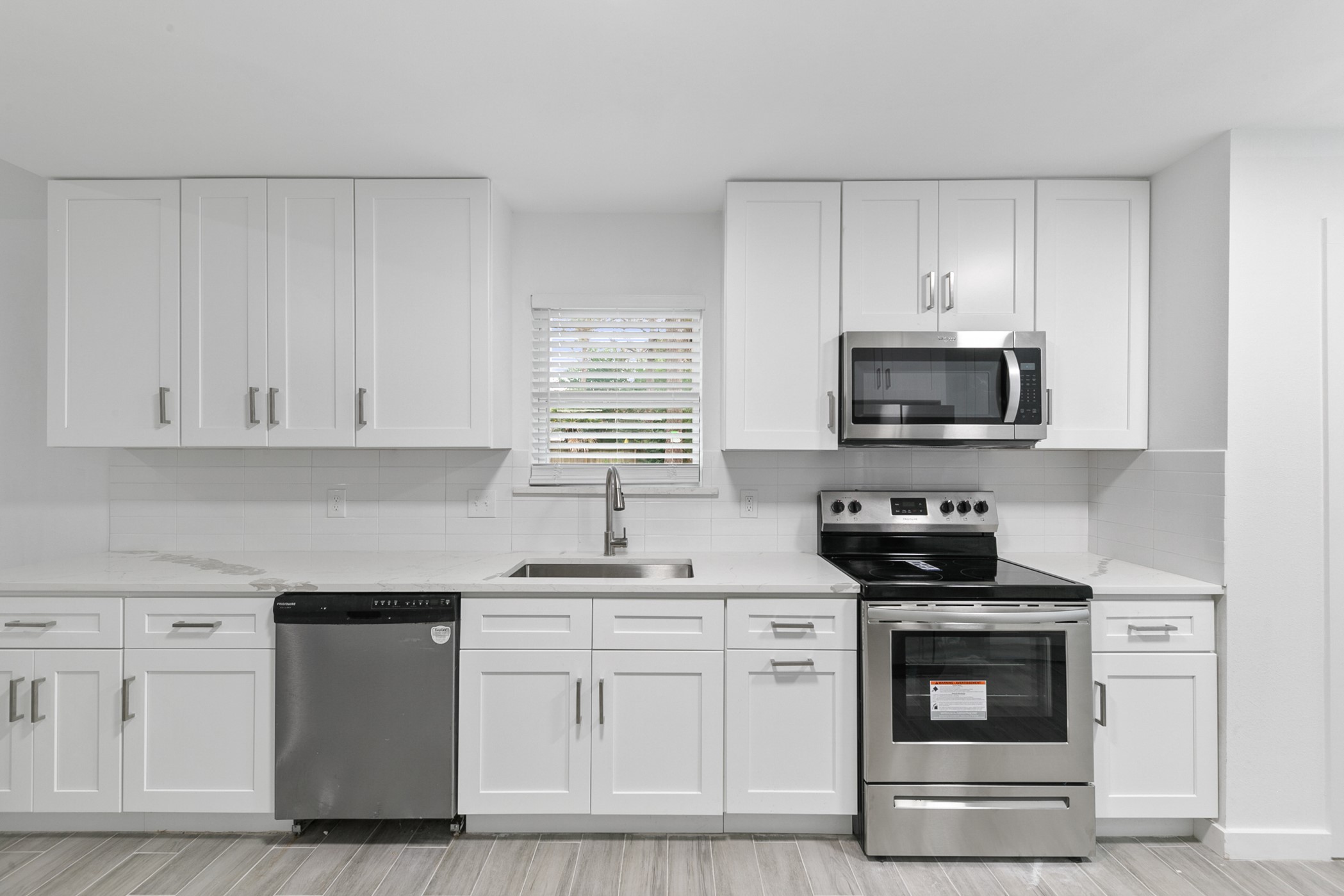 6811 McCullum Road Houston, TX 77489 - Photo 9 of 22 This modern kitchen features sleek white cabinetry, stainless steel appliances, and a neutral tile floor, creating a clean and inviting space.