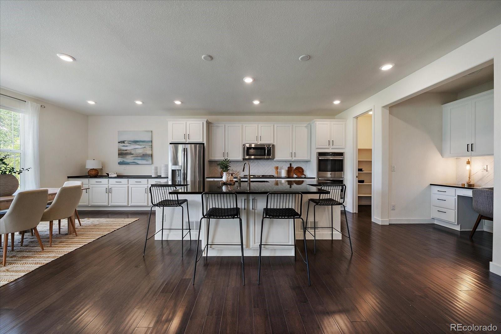 16062 Red Bud Loop Parker, CO 80134 - Photo 11 of 36 an open kitchen with kitchen island wooden floors wooden cabinets and stainless steel appliances