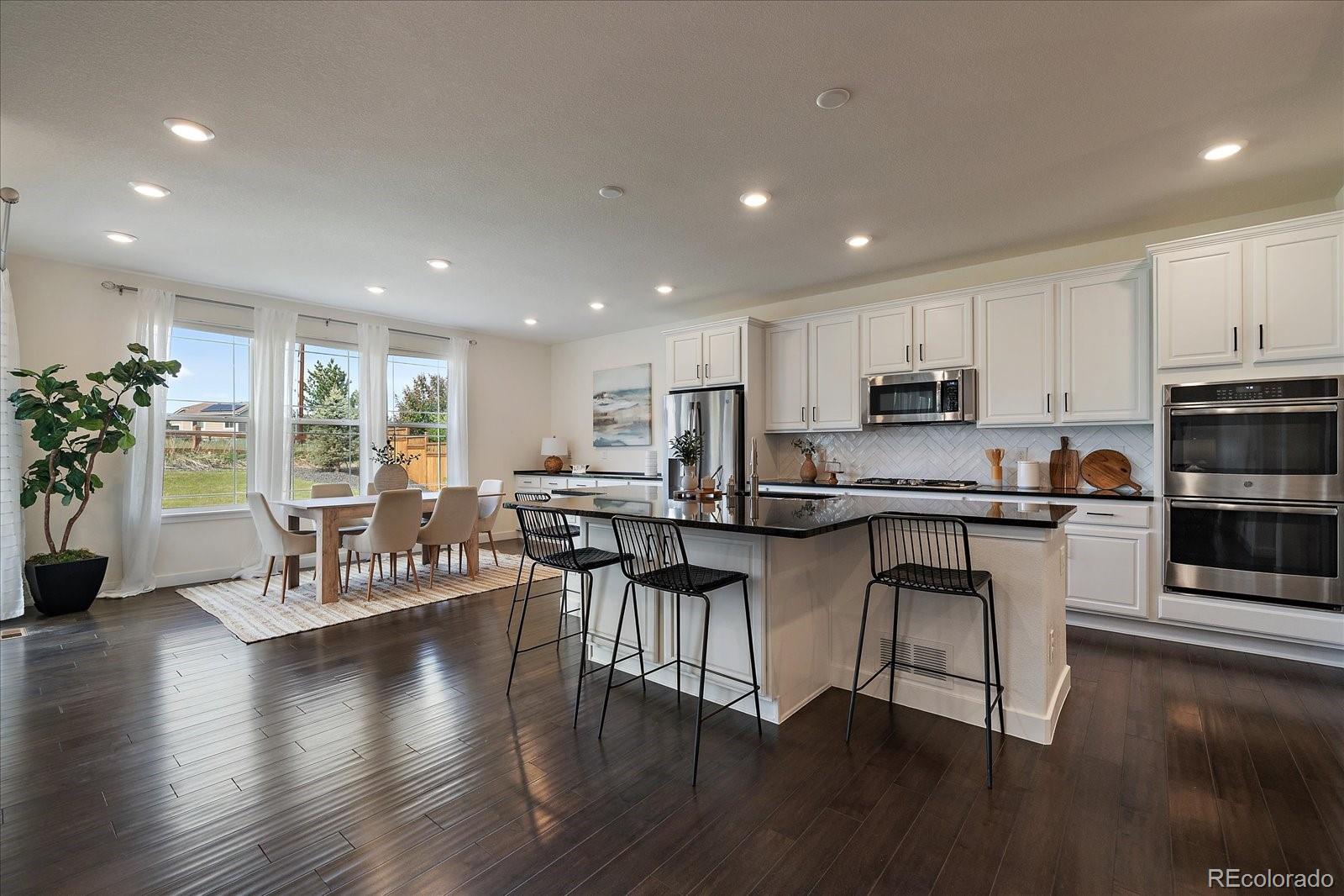 16062 Red Bud Loop Parker, CO 80134 - Photo 7 of 36 a open dining room with stainless steel appliances kitchen island furniture a wooden floor and a view of kitchen