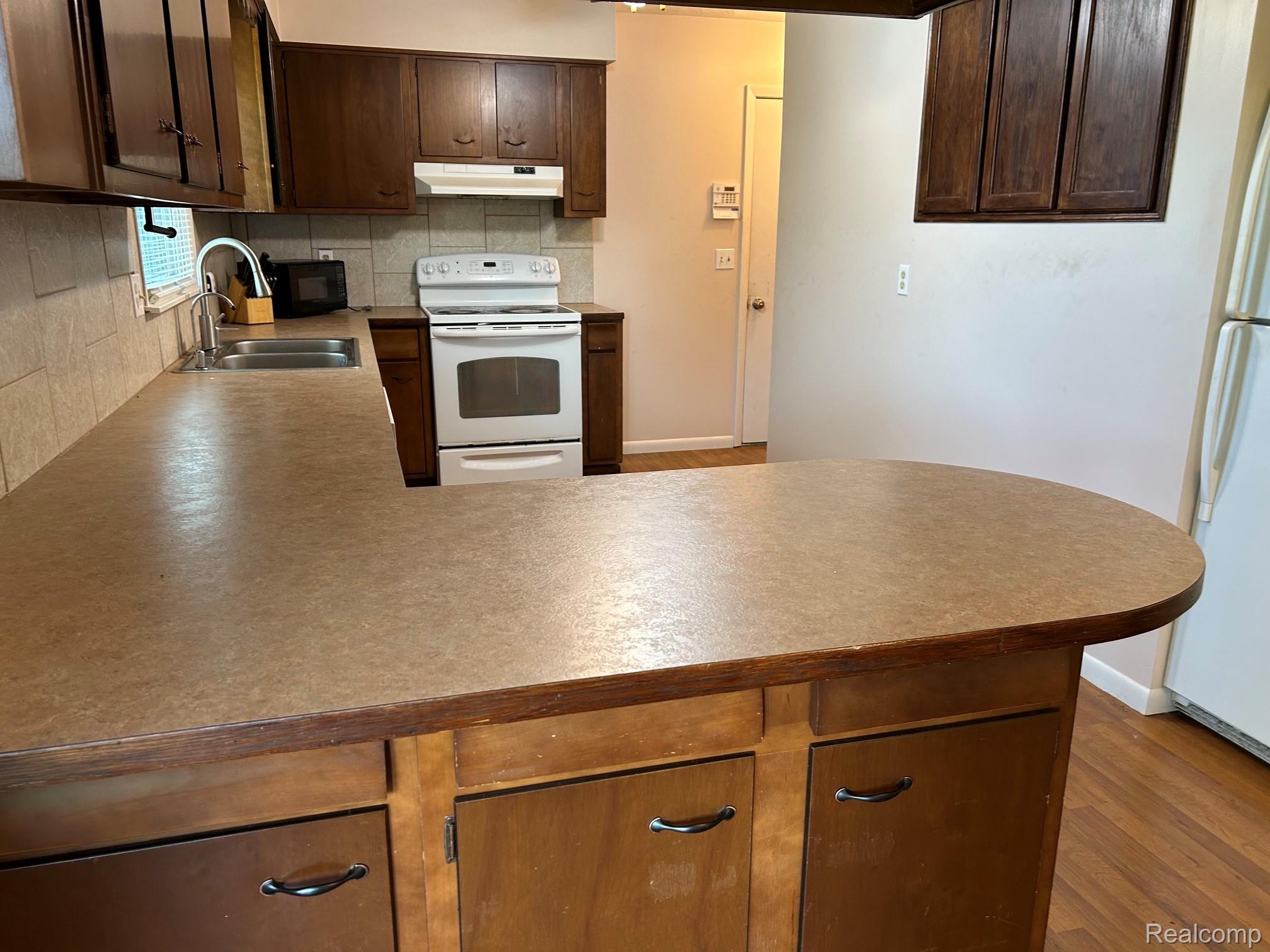 8233 West Iosco Road Fowlerville, MI 48836 - Photo 3 of 7 Kitchen featuring wood-finish cabinetry, a stainless steel sink, a tile backsplash, and a white range