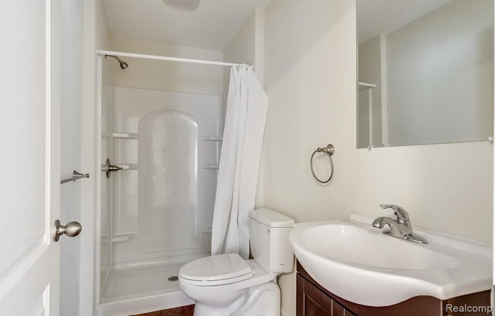 2365 Welch Road Walled Lake, MI 48390 - Photo 13 of 14 Full bathroom featuring a white shower stall with built-in shelving, a toilet, a vanity with a white integrated sink, and a wall-mounted mirror