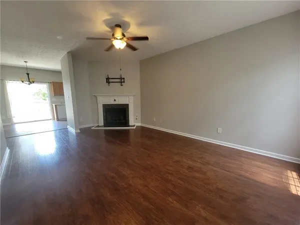 an empty room with wooden floor chandelier fan and windows